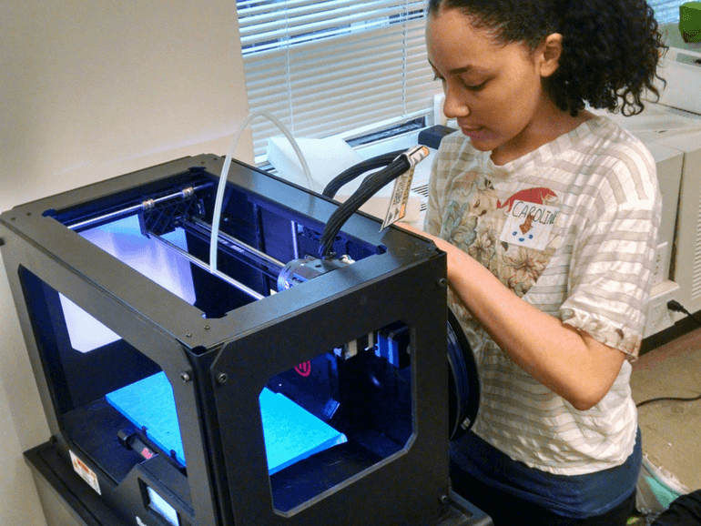 female student replacing filament roll located behind the printer